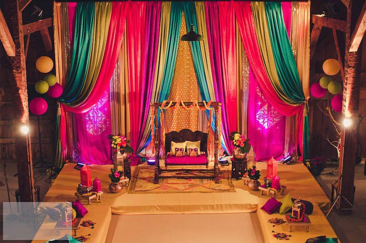 A vibrant wedding reception featuring a colorful backdrop, adorned with sparkling decorations and Bollywood-themed elements.