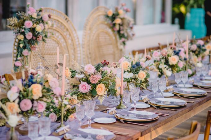 A long table adorned with a floral centerpiece and candles, set in a charming outdoor bohemian venue surrounded by greenery.